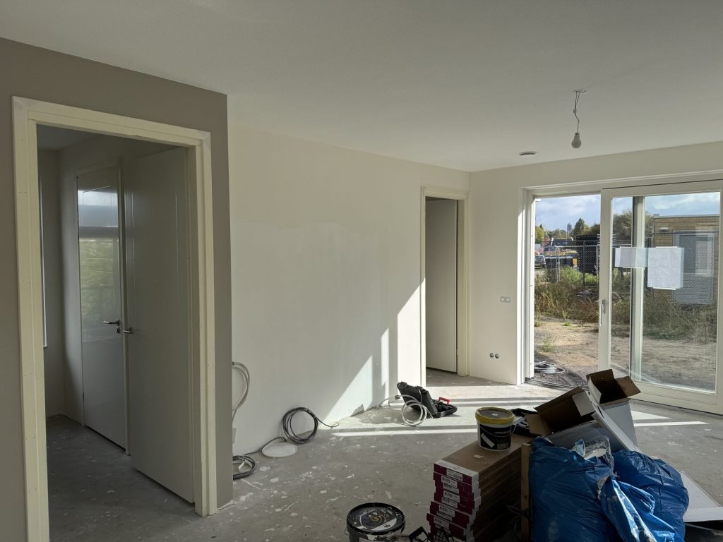 Opgeleverde nieuwbouwwoning met kale wanden en een pui naar de tuin, klaar voor de behanger