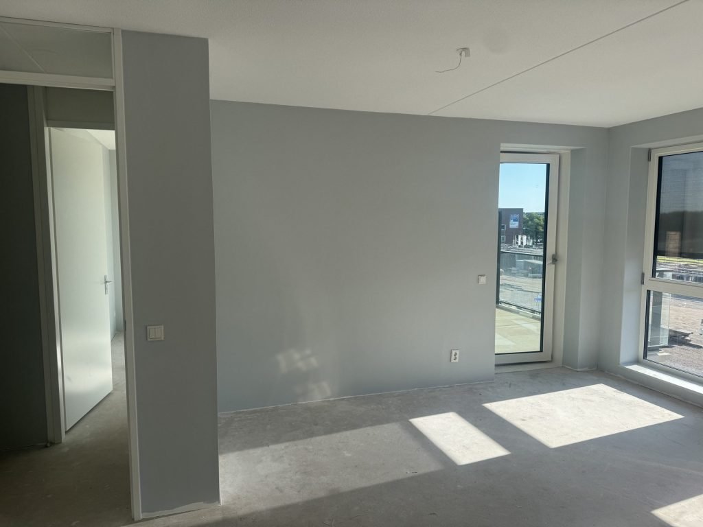 Lichtblauw gesausde wanden in een zonnig appartement met balkondeur, net na het plakken van renovlies