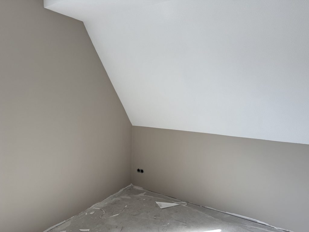 Zolderkamer met een schuine witte kap en rechte wanden in een warme zandkleur, pas afgewerkt