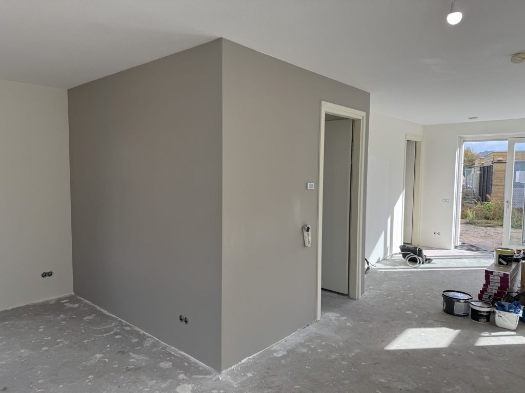 Woonkamer in een nieuw huis waar een losstaande wand grijs is gesausd over het vlies