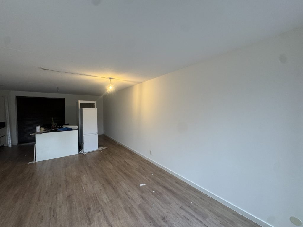 Lange woonkamer met open keuken en een strakke witte wand die net is behangen en gesausd